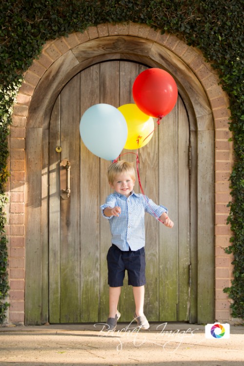 little kid holding colorful helium balloons like Curious George