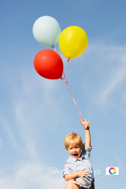 little kid holding colorful helium balloons like Curious George